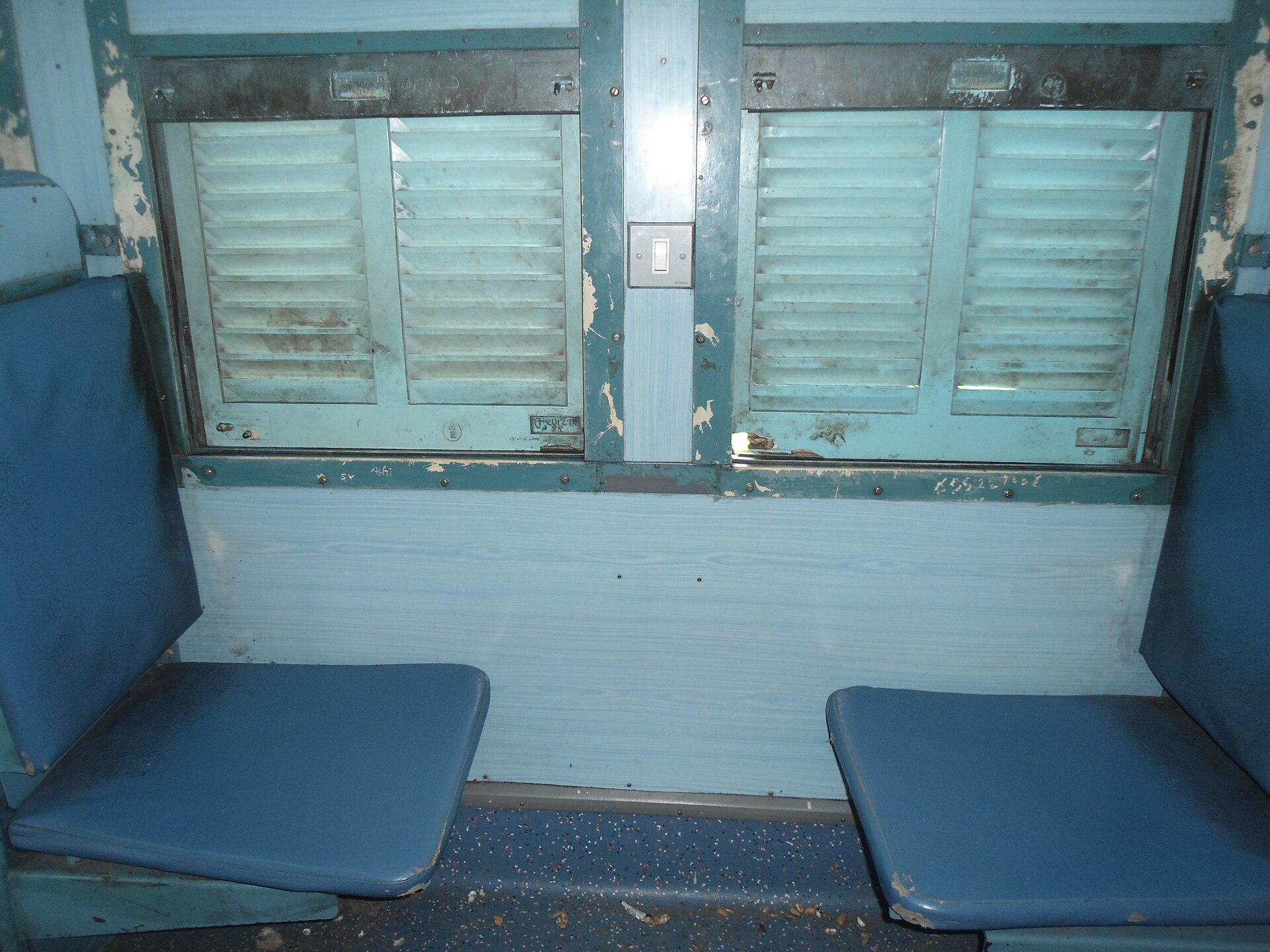 Empty blue seats beside shuttered windows inside an Indian passenger train coach