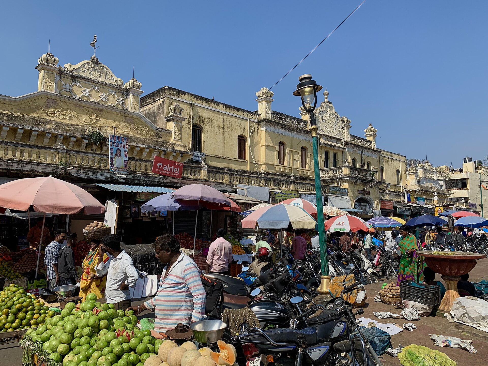 Fruit stalls under umbrellas outside the old Devaraja Market building in Mysuru