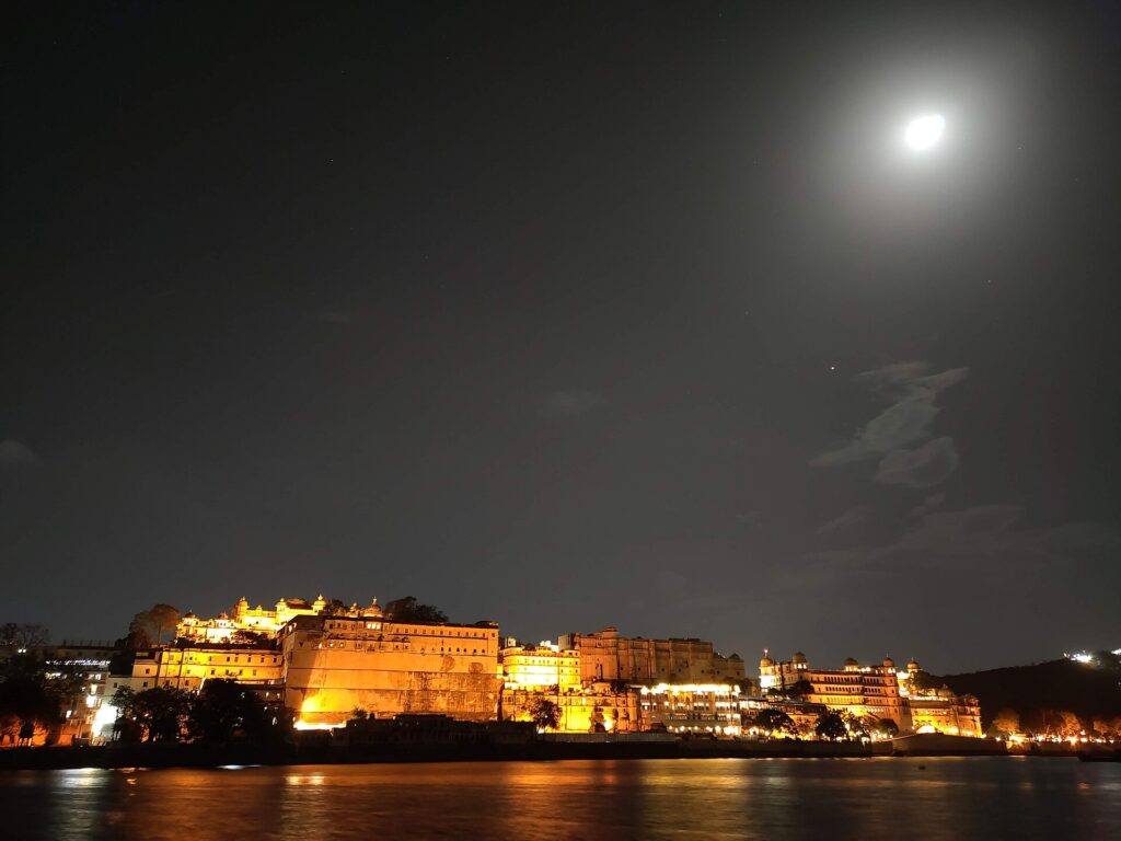 The illuminated City Palace reflected in Lake Pichola at night, seen from Ambrai Ghat