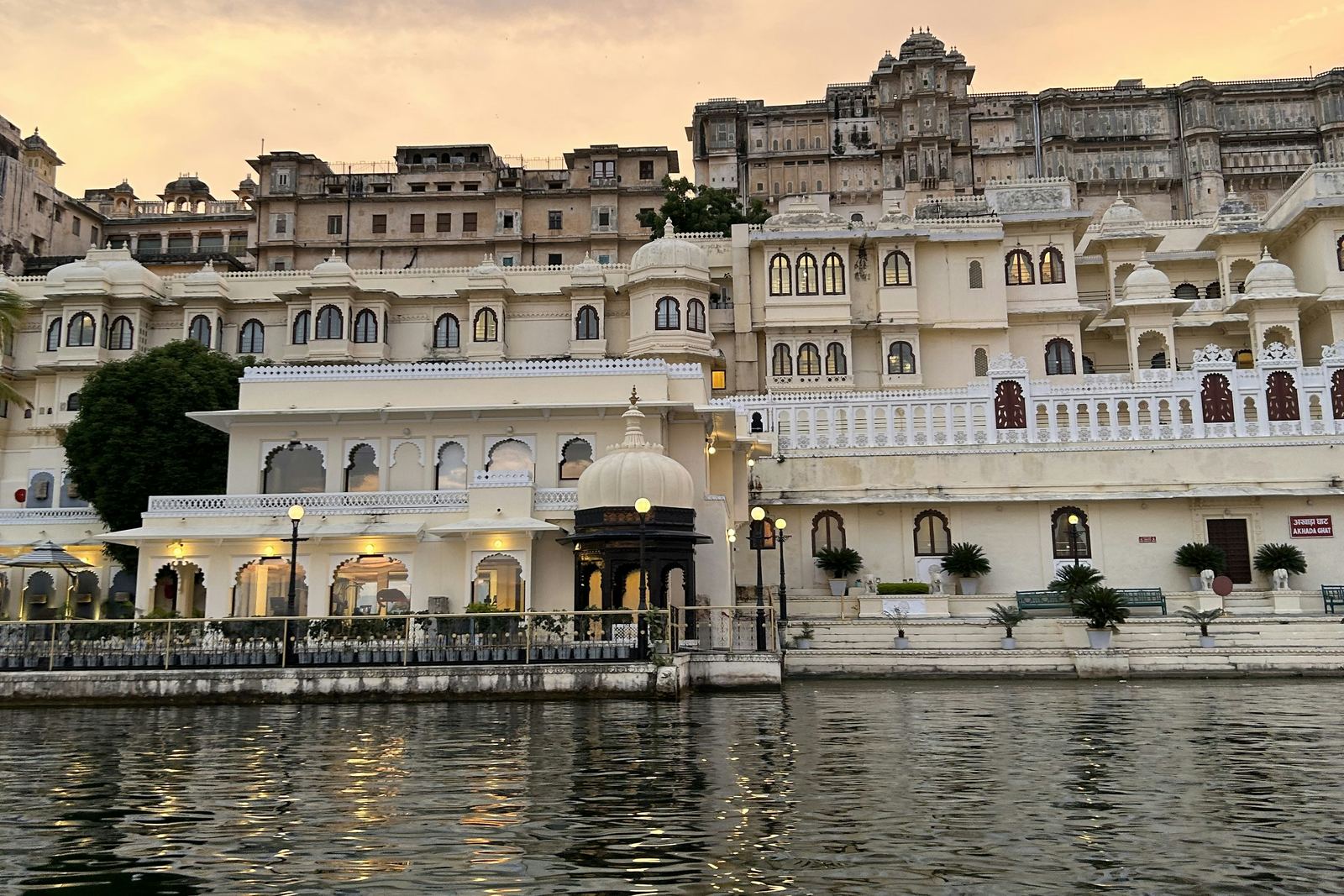 Lakeside facade of the City Palace complex in Udaipur glowing at dusk, seen from a boat on Lake Pichola