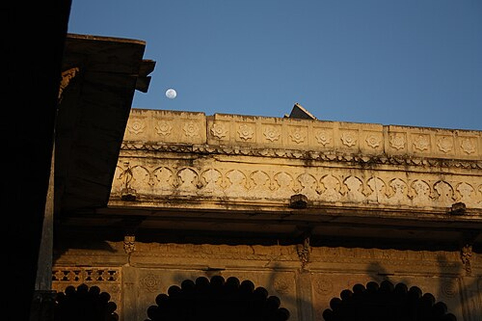 Moon rising over the carved roofline of the Bagore Ki Haveli courtyard at dusk