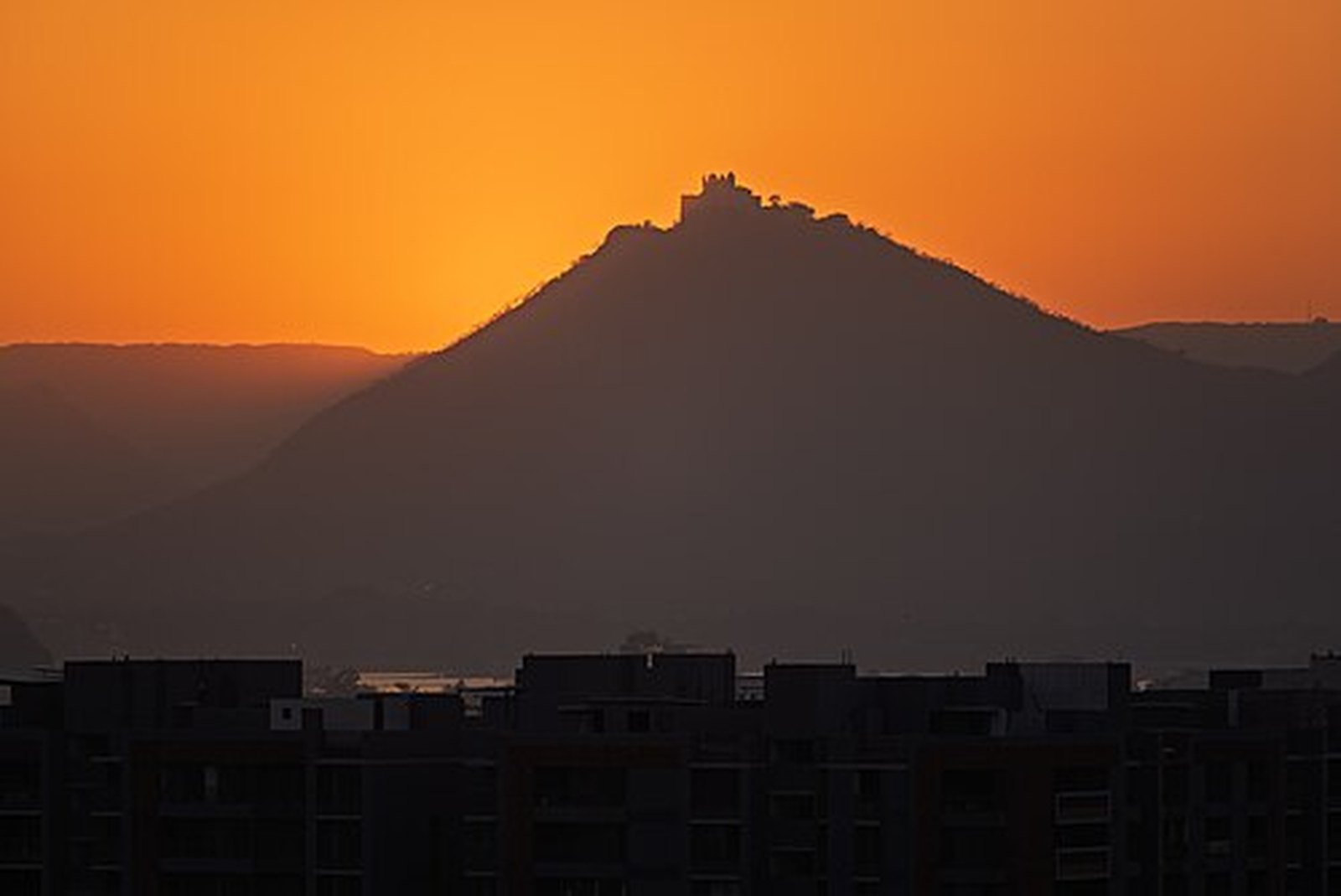 Sajjangarh Monsoon Palace silhouetted on its hilltop against an orange sunset